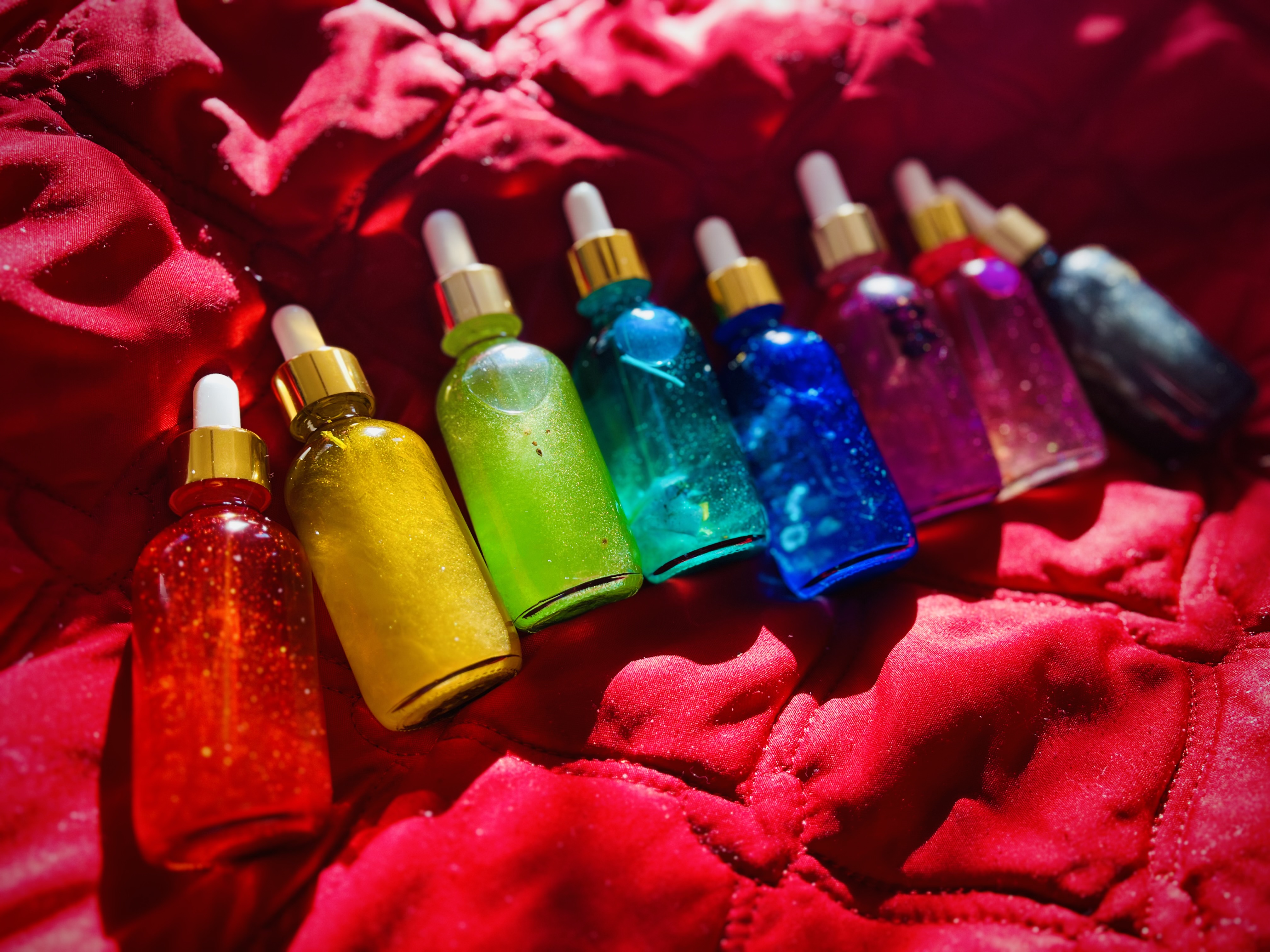 rainbow of handcrafted conjure oils in glass dropper bottles with gold caps, displayed on a wooden board