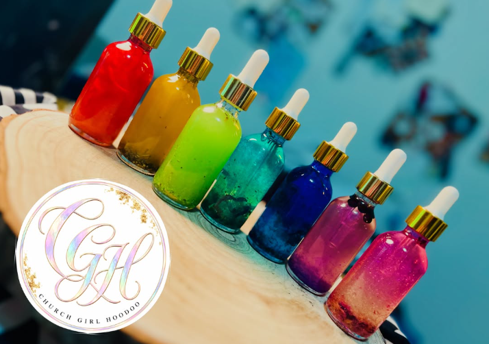 rainbow of handcrafted conjure oils in glass dropper bottles with gold caps, displayed on a wooden board